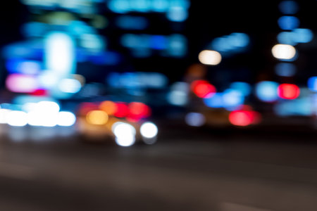 Blurred background with yellow taxi is moving fast on urban road among skyscrapers. Defocused illumination of buildings and moving car on night urban road.の写真素材