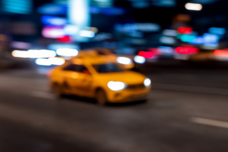 Blurred background with yellow taxi is moving fast on urban road among skyscrapers. Defocused illumination of buildings and moving car on night urban road.の写真素材