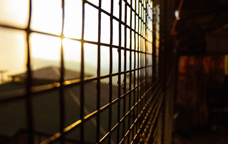 Sun shining through grid fences during a sunset symbolizing hope in captivity and other difficult and tough situations, 5Kの写真素材