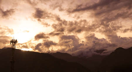 Silhouette Landscape of a communication tower and dramatic clouds which cover the mountains during a sunset.の写真素材