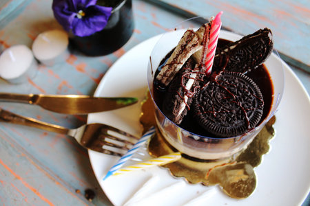 Chocolate cake with waffle and biscuits on top, sprinkled with nuts on a white plate. candles and...