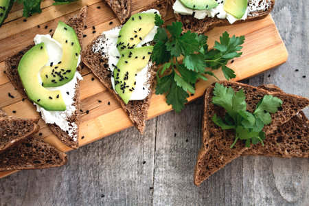 Sandwich with avocado, dark bread and white light cheese on wooden board