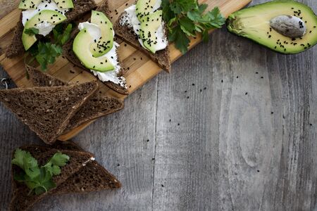 Sandwich with avocado, dark bread and white light cheese on wooden boardの写真素材