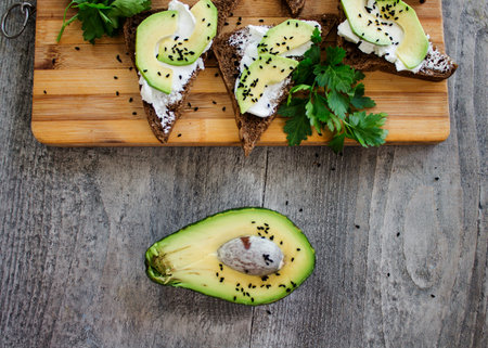 Sandwich with avocado, dark bread and white light cheese on wooden board
