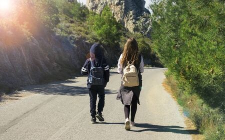 Friends with backpacks are walking along the mountain roadの写真素材