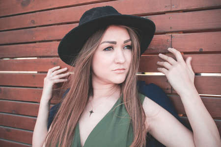 Young beautiful girl in a black hat and long dress on a brown wooden backgroundの写真素材