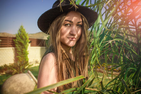 Young beautiful girl in a black hat and long dressin the sunny gardenの写真素材