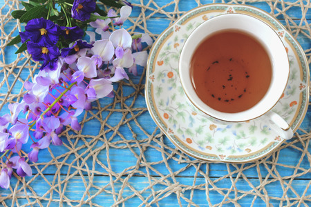 A cup of tea on a wooden blue table with a bouquet of colored field flowersの写真素材
