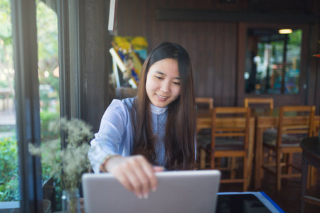 Women sitting and using smartphone and laptop on the table and she is feeling happiness at garden or...