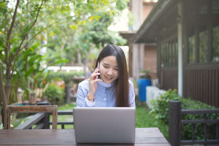 Women sitting and using smartphone and laptop on the table and she is feeling happiness at garden or cafe shop.の写真素材