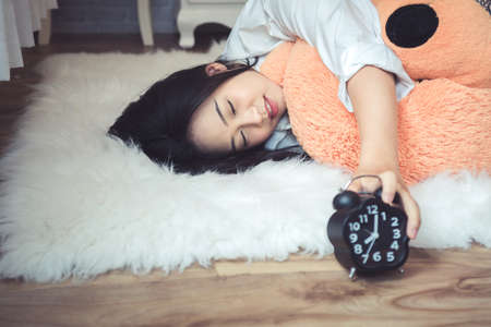 Beautiful young asian woman lying in bed in the morning. She is waking up with alarm clock.の写真素材