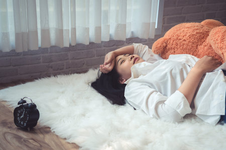 Beautiful young asian woman lying in bed in the morning. She is waking up with alarm clock.