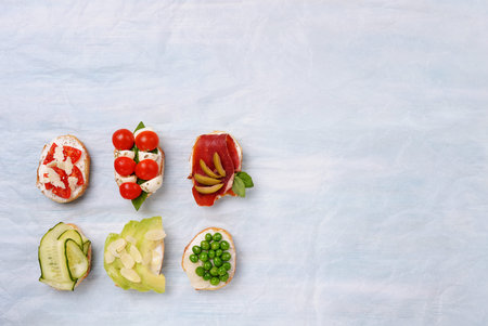 Various canapes or tapas with vegetables, cheese, salmon, ham on the blue background.Top view with...