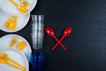 Bright plastic disposable tableware. Ecology concept with colorful single use  cutlery , 
cups , plates  on black background. Environmental concept..Plastic waste danger concept.の写真素材