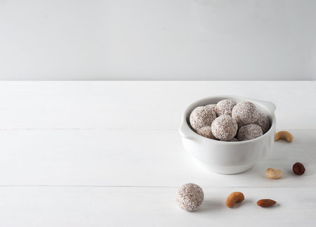Vegan sweets.Image of healthy energy balls with nuts, coconuts chips and dry fruits.White plate on the white wooden background. Selective focus.Horizontal orientation.の写真素材