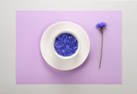 Creative layout made of blue petals of cornflower floating in water on light  lilac pastel background laying on the gray table.Flat lay, concept with copy space for lettering,text or design.の写真素材
