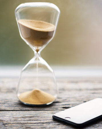 Image of a mobile phone and sand clock . Concept of limiting time spending on your devices.Time...