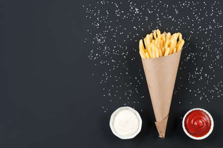 Tasty french fries from potato with sauces ketchup and mayonnaise over black background. Fries in the paper cone.の写真素材
