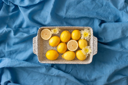 Summer arrangement with lemons and yellow flowers in a water bath on a blue linen beach towel....