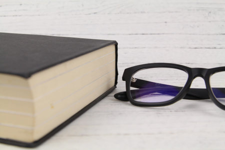 Close up Black Eye Glasses with a thick black book over wooden texture background. Copy Space conceptの写真素材