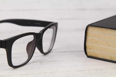 Close up Black Eye Glasses with a thick black book over wooden texture background. Copy Space...