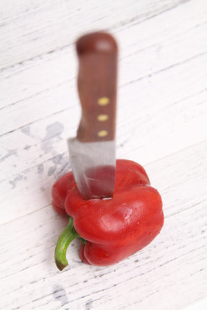 Fresh red bell capsicum peppers with a knife on a bright wooden background. Cooking concept