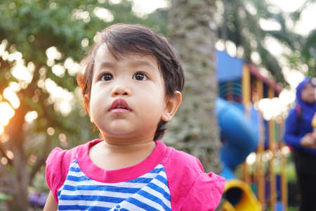 Potrait of Cute Asian Kid Girl on outdoor playground in the evening over sun ray background. Summer Leisure for kidsの写真素材