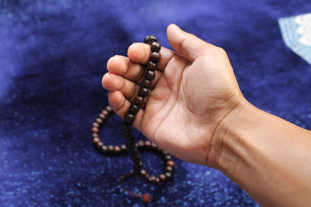Hand holding a muslim beads rosary or tasbih on a praying mat, pray to god. Ramadhan Kareem