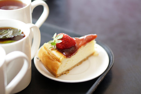 Slice of cheese Cake with cream and fresh strawberries on plate with a cup of tea over blur...