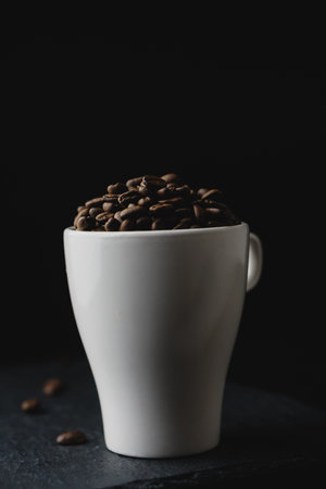 Coffee bean on a white cup over a rock stone slate. Black dark background. Celebrating Coffee...