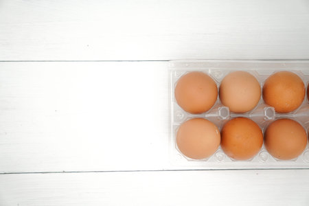 Close-up view of raw chicken eggs in egg box on white wooden background