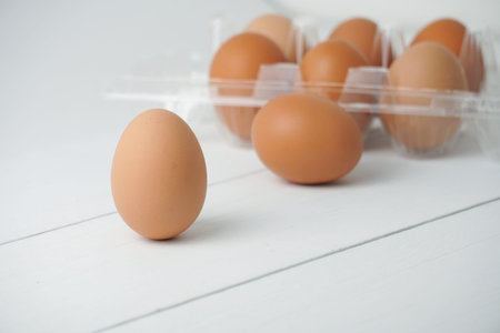 Close-up view of raw chicken eggs in egg box on white wooden background