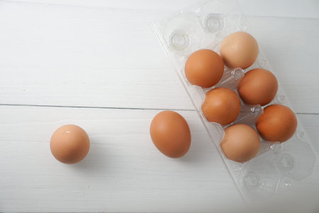 Close-up view of raw chicken eggs in egg box on white wooden background