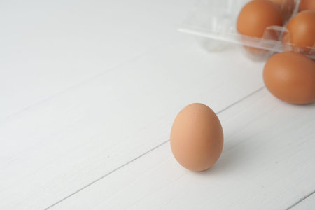 Close-up view of raw chicken eggs in egg box on white wooden background