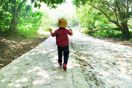 Perspective view from back of a cute little girl run on a walk path inside a forest with light flares. Freedom and carefree. Happy childhood.の写真素材
