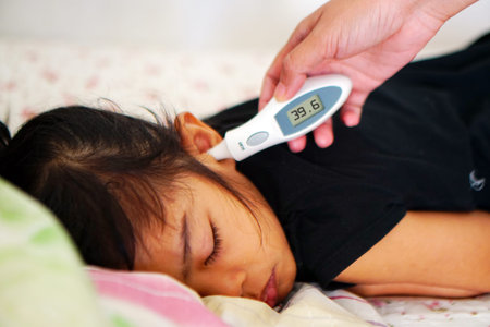 Mother measuring temperature of her ill kid girl.Sick child with high fever laying in sofa and mother holding thermometer.Clinical digital ear thermometer scan in hand of a physicianの写真素材