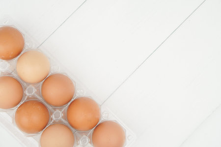 Close-up view of raw chicken eggs in egg box on white wooden background