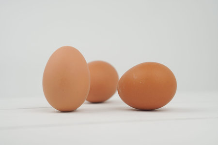 Close-up view of raw chicken eggs in egg box on white wooden background