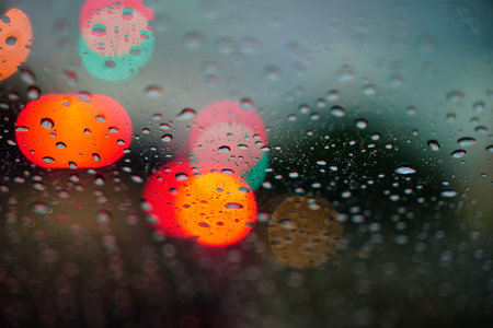 Traffic light bokeh with rain drops. Reflections of raindrops on glass on car window. Raindrops drizzle on glass window at night.の写真素材