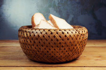 Slices of bread in wicker breadbasket on wooden tableの写真素材