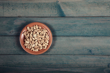 Roasted salted peanuts in plate on old wooden table