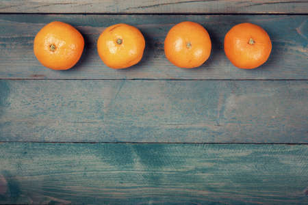 Row of four tangerine (mandarin) on old, blue wooden background, top viewの写真素材
