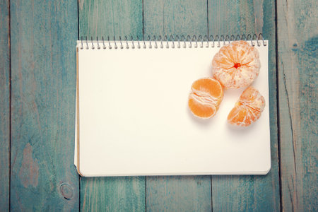 Slices of tangerine (mandarin) with blank notebook on wooden backgroundの写真素材