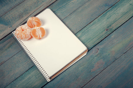 Slices of tangerine (mandarin) with blank notebook on wooden background