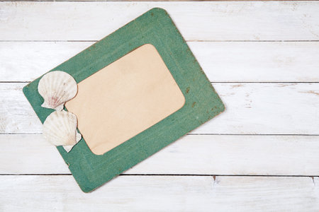 Old green photo frame with two sea shells on white wooden backgroundの写真素材
