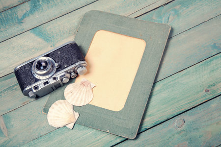 Old green photo frame with two sea shells and vintage camera on wooden backgroundの写真素材