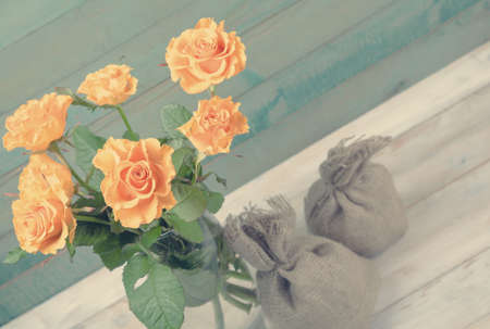 Bouquet of yellow roses in glass vase with two burlap bags over old wooden backgroundの写真素材