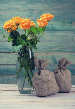 Bouquet of yellow roses in glass vase with two burlap bags over old wooden backgroundの写真素材