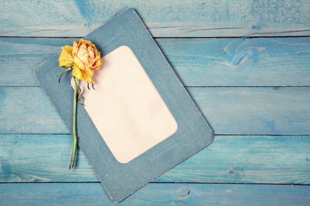 One dried yellow rose with blank photo frame on old blue wooden background