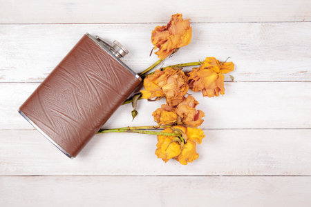 Hip flask with dryed roses on old, white wooden background